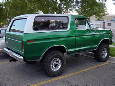 1979 Ford Bronco - A lifted green Ford Bronco with a white hardtop is parked in a lot, showing its side and rear profile.