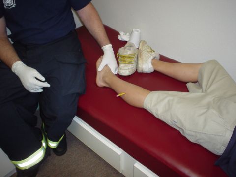 1990 Ford Bronco - A person lies on a red examination table while a paramedic checks their leg, which has a pencil embedded in it.