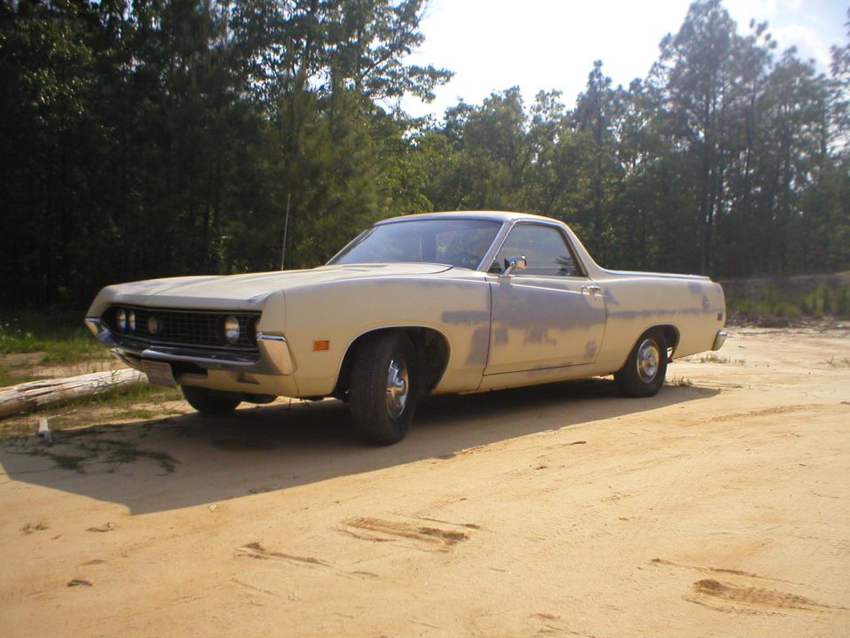 Cream 1970 Ford Ranchero with faded paint parked on sandy dirt lot, front three-quarter view