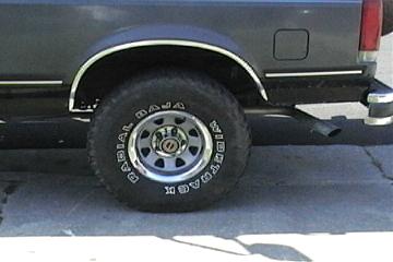 1989 Ford Bronco - Close-up of the rear wheel and fender of an SUV, showing the tire and exhaust pipe.