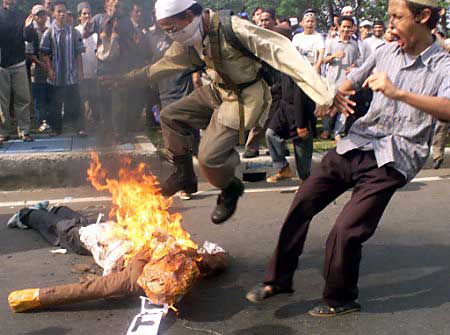 1990 Ford Bronco - A group of people are gathered on a street, with two men in the foreground appearing to stomp on and kick a burning effigy that is lying on…