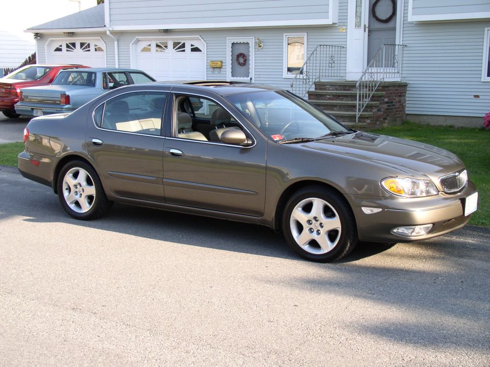 Brown Infiniti I30 sedan, 3/4 front view. Other cars and house in background