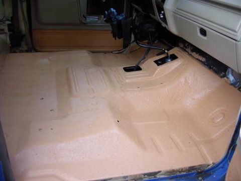 1980 Ford Bronco - Vehicle interior floor coated with tan spray-on bedliner, showing the transmission tunnel and pedals.