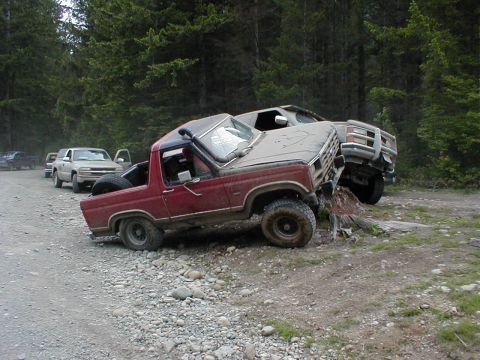 1983 Ford Bronco - This red SUV is wedged on a log, with another vehicle close behind it on a dirt road.