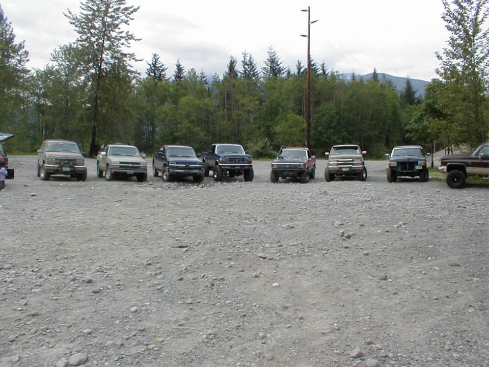 Line of pickup trucks and SUVs parked on gravel