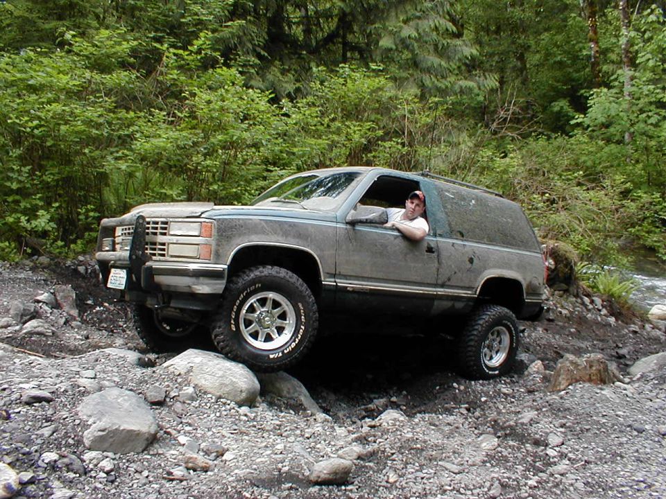 Gray SUV with brush guard navigating a rocky trail, driver visible
