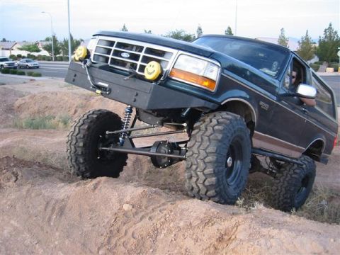 1994 Ford Bronco - Modified Ford Bronco with oversized tires navigates a dirt obstacle.