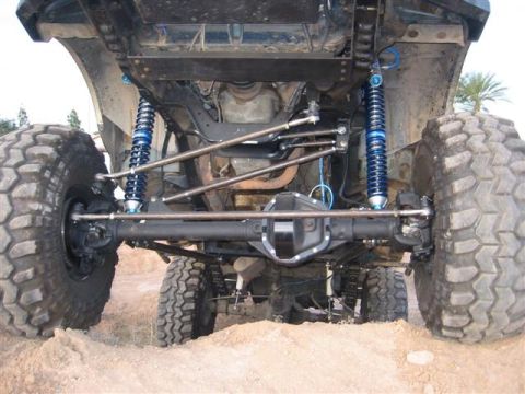 1994 Ford Bronco - The underside of a heavily modified SUV, large off-road tires and vibrant blue suspension components, is captured in this image.