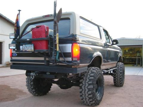 1994 Ford Bronco - This modified 1994 Ford Bronco features oversized tires, a rear-mounted fuel can, and a shovel, ready for off-road adventures.