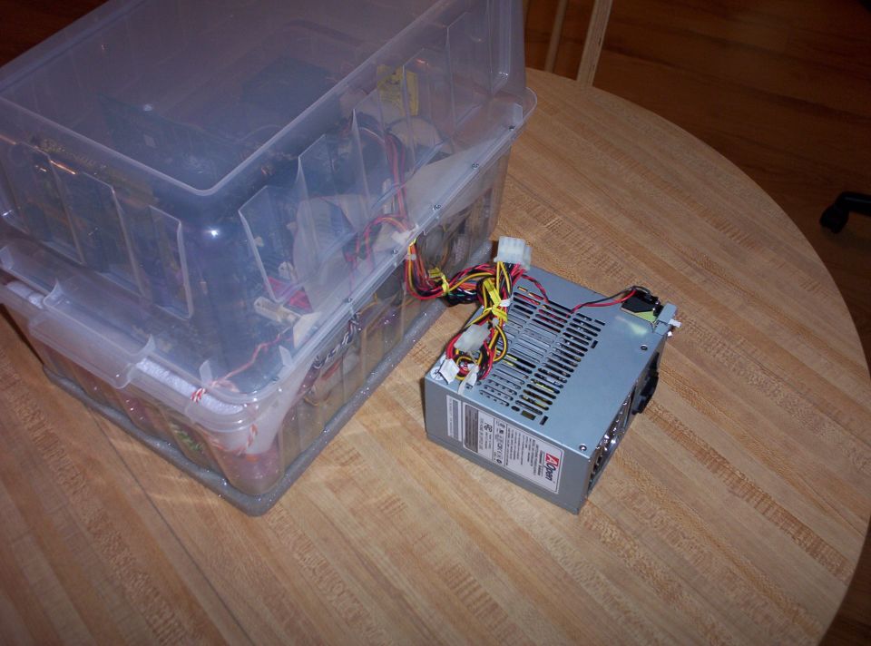 Computer parts in clear plastic bins wired to an AOpen power supply on a wooden table