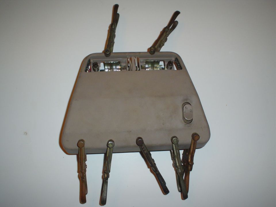 Removed automotive overhead console with mirror and wiring sitting on clothespins against a wall