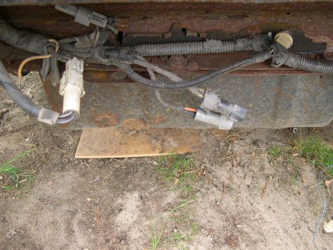 1994 Ford Bronco - Close-up view of electrical wiring and connectors attached to a rusty vehicle frame.