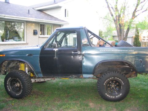 1986 Ford Bronco - Modified Ford Bronco with roll cage and custom paint. A child sits in the passenger seat.