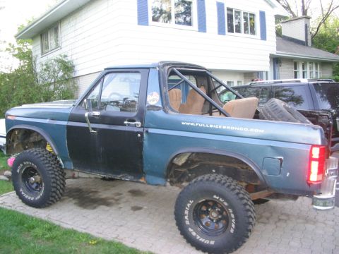 1986 Ford Bronco - Modified Ford Bronco with roll cage and large tires parked in a driveway. Another vehicle is behind it.