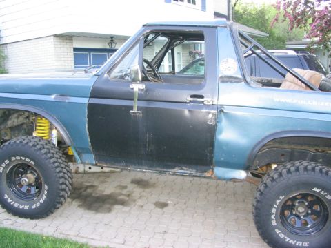 1986 Ford Bronco - This modified Ford Bronco features a roll cage and oversized tires, with another vehicle visible in the background.