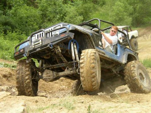 1995 Ford Bronco - A heavily modified Jeep Wrangler navigates a muddy off-road trail with another vehicle following behind.