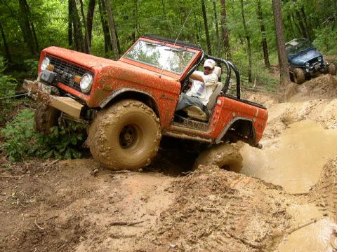 1995 Ford Bronco - An orange off-road vehicle navigates a muddy trail with another vehicle in the background.