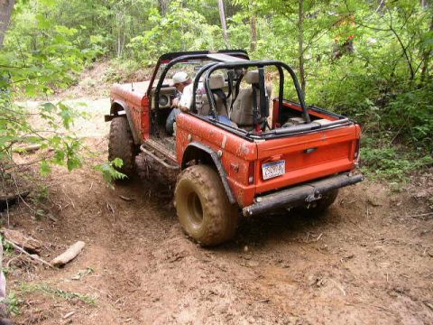 1995 Ford Bronco - This Ford Bronco is navigating a challenging off-road trail covered in mud and surrounded by trees.