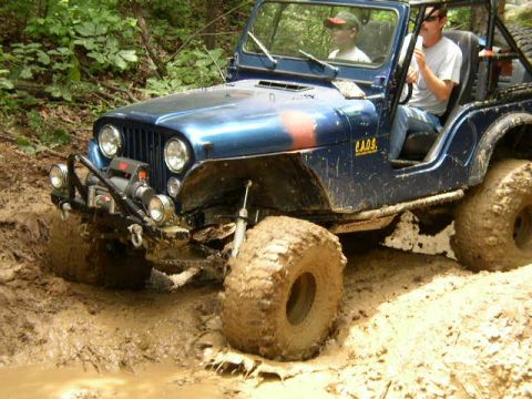 1995 Ford Bronco - A blue Jeep Wrangler navigates a muddy trail with its front end partially submerged in the muck.