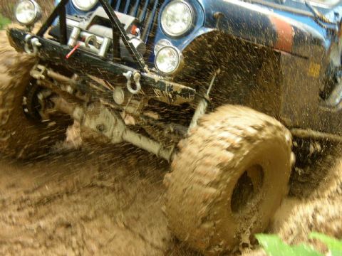 1995 Ford Bronco - Off-road vehicle navigates a muddy terrain, kicking up significant spray.
