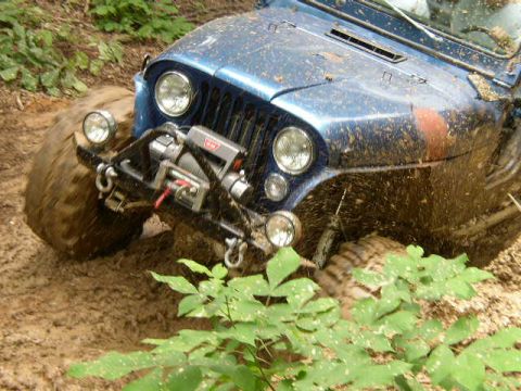 1995 Ford Bronco - A blue Jeep Wrangler is deeply stuck in mud, with its tires caked and mud splattering the body.