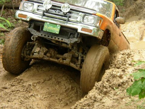 1995 Ford Bronco - This orange SUV, possibly a 1995 model, tackles a challenging muddy terrain with its large off-road tires.