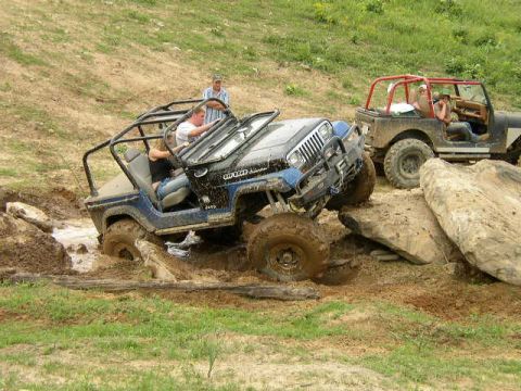 1995 Ford Bronco - Off-road vehicles tackle a challenging muddy terrain with large boulders.