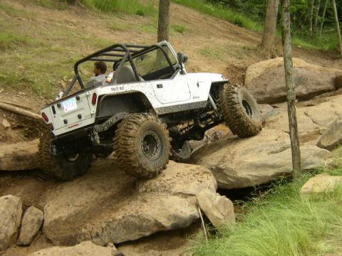 1995 Ford Bronco - White Jeep Wrangler navigates a rocky off-road trail with large tires.