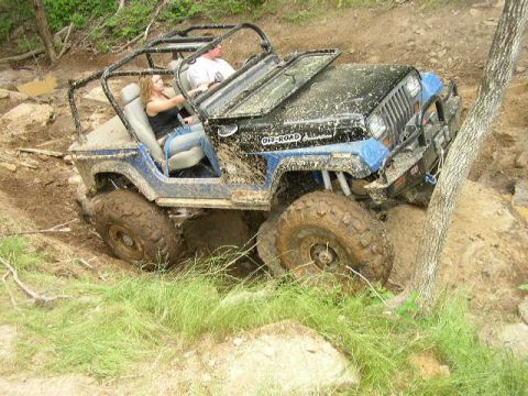 1995 Ford Bronco - A modified Jeep Wrangler navigates a challenging off-road course, covered in mud.