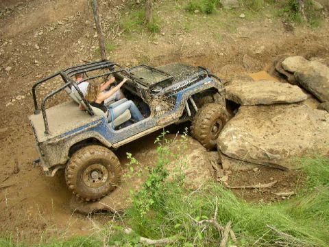1995 Ford Bronco - A blue Jeep Wrangler is shown off-roading through mud and rocks.