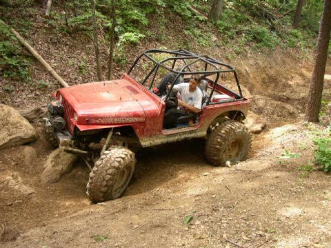 1995 Ford Bronco - A modified red jeep tackles a challenging off-road course with steep inclines and rocky terrain.