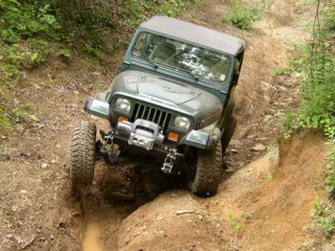 1995 Ford Bronco - A green Jeep Wrangler navigates a challenging off-road trail, its front tire high on a ledge.