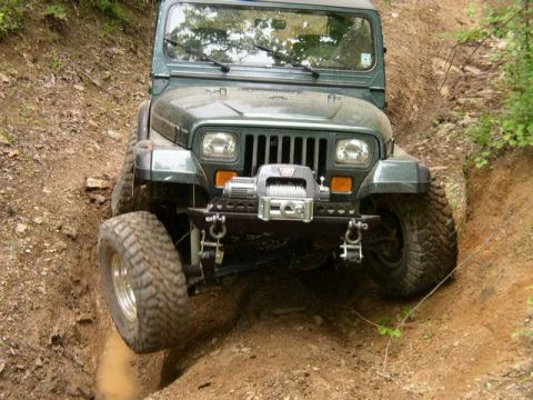 1995 Ford Bronco - Jeep Wrangler with winch is off-roading on a dirt trail.