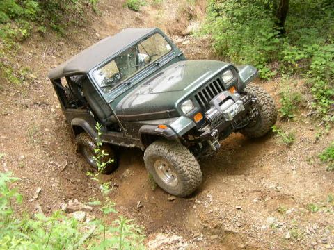 1995 Ford Bronco - A Jeep Wrangler navigates a steep, muddy off-road trail.