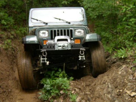 1995 Ford Bronco - A green Jeep Wrangler navigates a challenging muddy off-road trail.