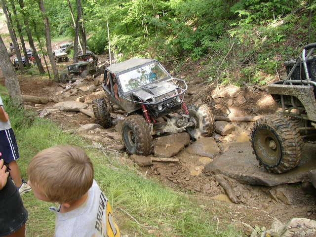 off-road buggy navigating a rocky, muddy trail with other vehicles in the background