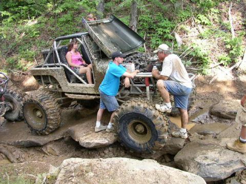 1995 Ford Bronco - People interact with a heavily modified off-road vehicle stuck in mud and rocks.