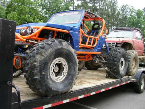 1995 Ford Bronco - Two heavily modified off-road vehicles are transported on a flatbed trailer.