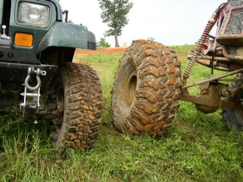 1995 Ford Bronco - A close-up view of the front tire and suspension of a green off-road vehicle, with another vehicle visible to the right.
