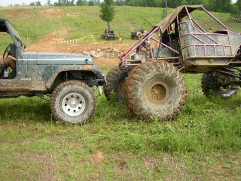 1995 Ford Bronco - Two custom off-road vehicles are parked on a grassy area with hills in the background.