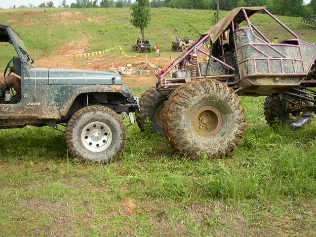 Green Jeep parked next to a custom-built buggy with large tires on a grassy field