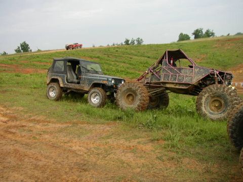1995 Ford Bronco - Two off-road vehicles are parked on a grassy and muddy terrain under a cloudy sky.