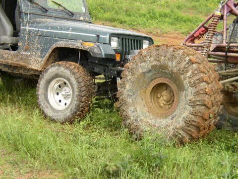 1995 Ford Bronco - A muddy green Jeep Wrangler is parked next to another off-road vehicle, highlighting their large tires and suspension systems.