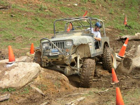 1995 Ford Bronco - A Jeep Wrangler tackles a challenging off-road course marked by orange cones and large rocks.