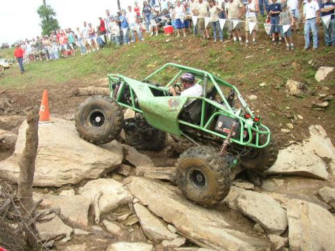 1995 Ford Bronco - A custom-built green off-road buggy navigates a rocky incline with spectators in the background.