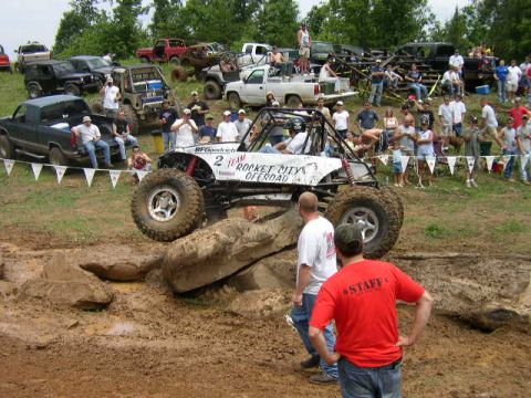 1995 Ford Bronco - A custom-built off-road buggy tackles a challenging mud and rock obstacle course with spectators watching.