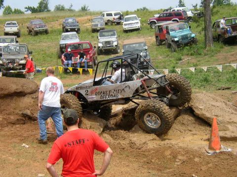 1995 Ford Bronco - An off-road buggy navigates a challenging dirt obstacle course with spectators and other vehicles nearby.
