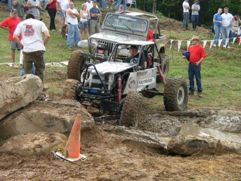 1995 Ford Bronco - Two off-road vehicles navigate a muddy obstacle course with spectators watching.