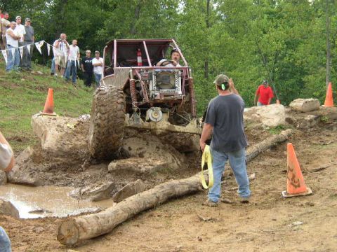 1995 Ford Bronco - An off-road buggy navigates a muddy obstacle course, with spectators watching from a grassy embankment.