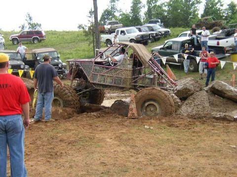 1995 Ford Bronco - A custom-built buggy is stuck deep in the mud during an off-road event, with spectators and other vehicles nearby.